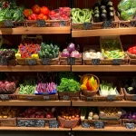 Frisches Obst und Gemüse in Körben, ordentlich auf Regalen eines Supermarkts präsentiert.